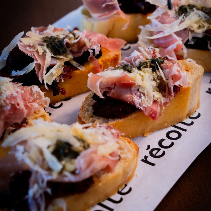 Bruschettas di Parma com presunto parma, parmesão e pesto, sobre o papel do Récolte