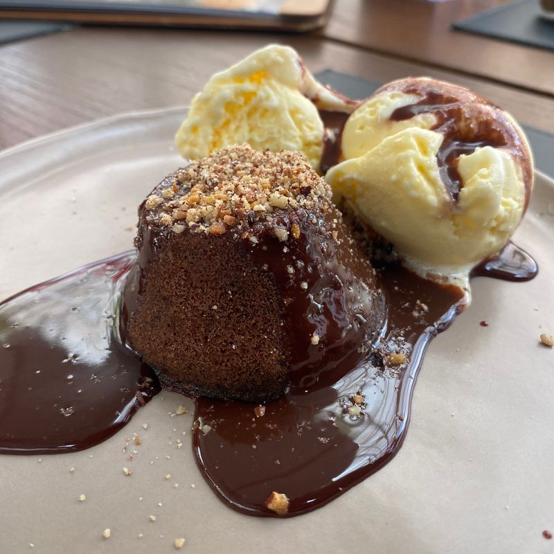 Petit gâteau com duas bolas de sorvete de creme, calda de chocolate e farofa de castanhas