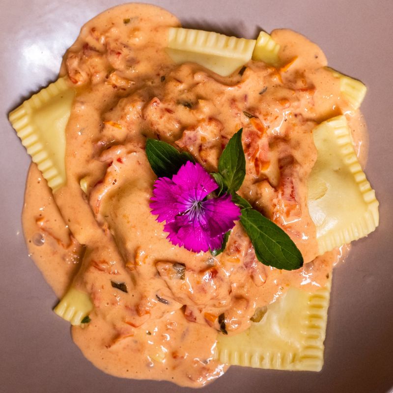 Ravióli ao molho rosé com flor comestível e folhas de manjericão, visto de cima