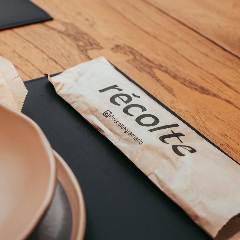 Envelope de talheres com a marca récolte e o Instagram @recoltegramado sobre a mesa de madeira